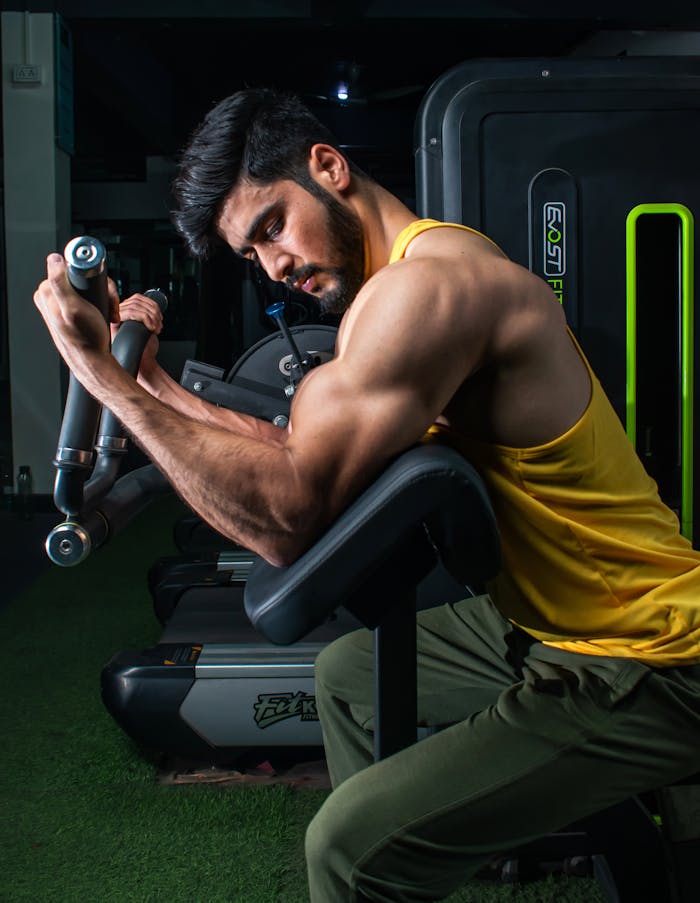 about-us Muscular man in a gym performing bicep curls on a machine, showcasing strength and dedication.